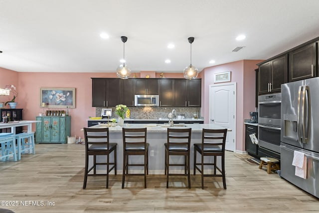 kitchen with appliances with stainless steel finishes, decorative backsplash, dark brown cabinetry, pendant lighting, and an island with sink