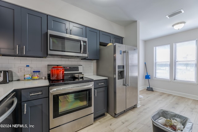 kitchen with decorative backsplash, appliances with stainless steel finishes, and light hardwood / wood-style flooring