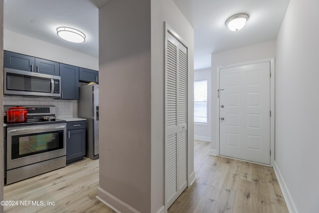 kitchen with blue cabinets, light wood-type flooring, backsplash, and appliances with stainless steel finishes