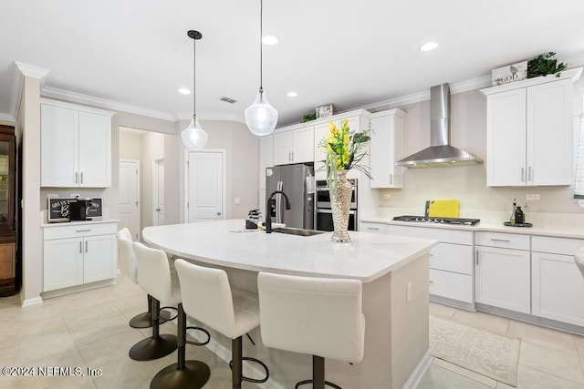 kitchen featuring wall chimney exhaust hood, sink, a center island with sink, white cabinets, and hanging light fixtures