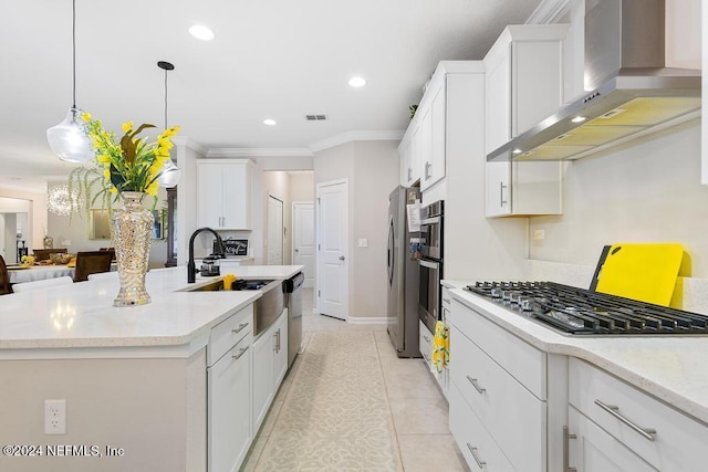 kitchen featuring wall chimney exhaust hood, crown molding, decorative light fixtures, a center island with sink, and appliances with stainless steel finishes