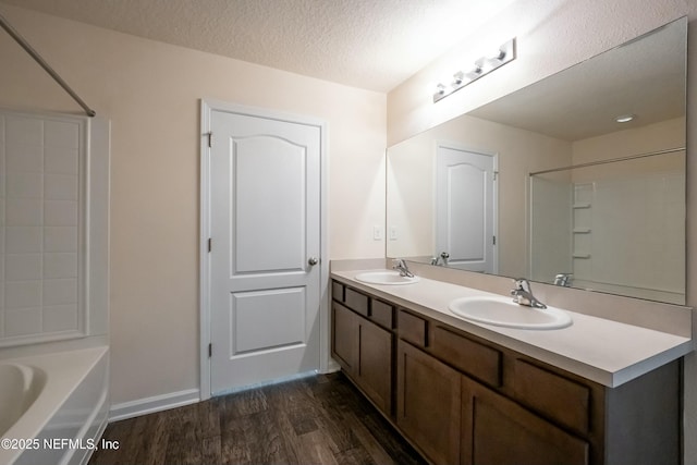 full bath with a textured ceiling, double vanity, wood finished floors, and a sink