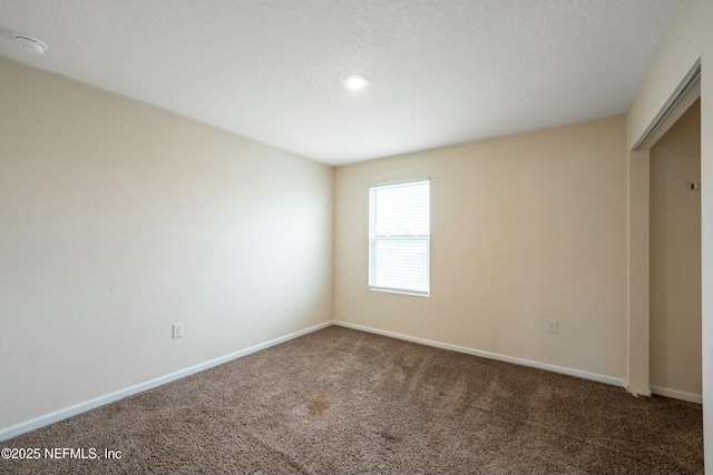 unfurnished room with dark carpet and baseboards