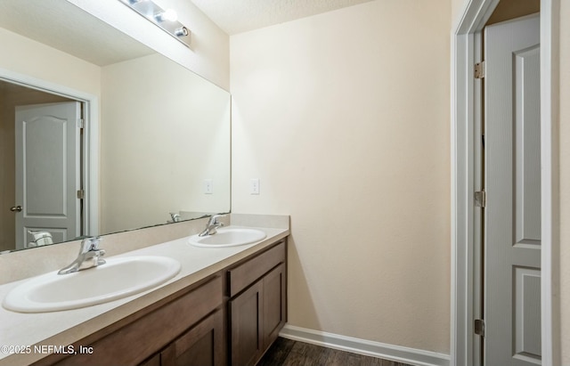 bathroom featuring double vanity, wood finished floors, a sink, and baseboards