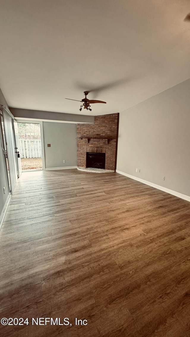 unfurnished living room with hardwood / wood-style flooring, a brick fireplace, and ceiling fan