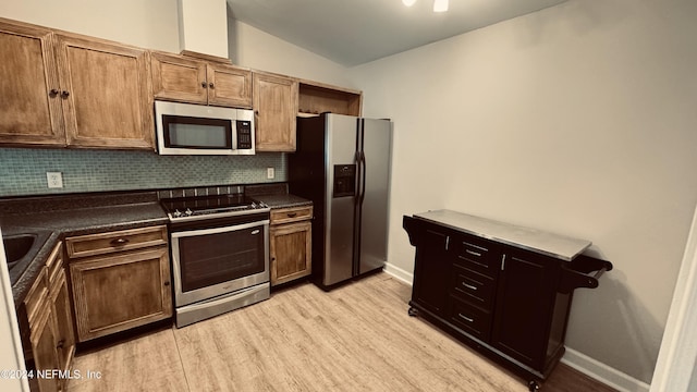 kitchen featuring backsplash, light wood-type flooring, stainless steel appliances, and vaulted ceiling