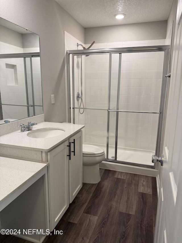 bathroom with vanity, hardwood / wood-style flooring, toilet, a textured ceiling, and an enclosed shower