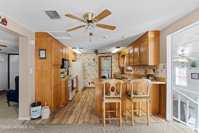 kitchen featuring sink, kitchen peninsula, light hardwood / wood-style floors, white appliances, and a kitchen bar