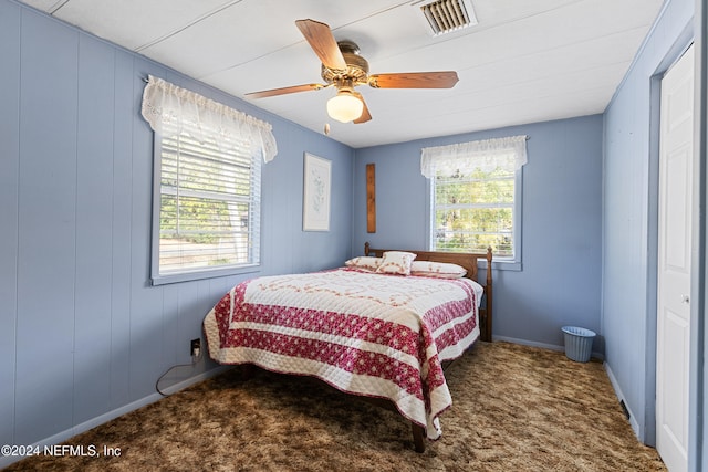 carpeted bedroom featuring multiple windows, wood walls, and ceiling fan