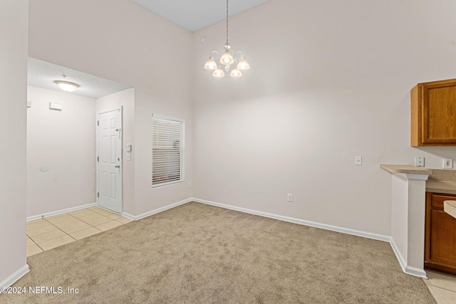 unfurnished dining area featuring a chandelier, a towering ceiling, and light colored carpet