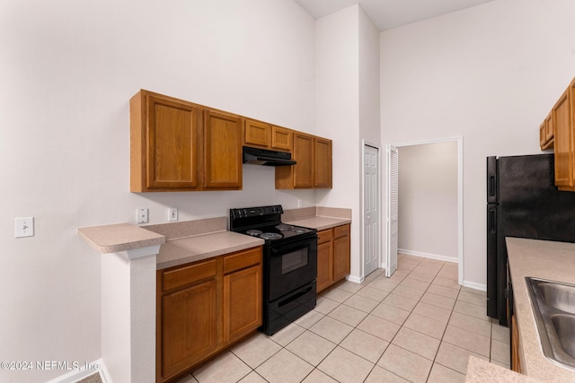 kitchen featuring sink, light tile patterned flooring, black appliances, and a high ceiling