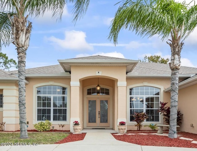 view of exterior entry with stucco siding, french doors, and roof with shingles