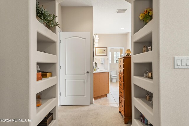 hallway featuring light tile patterned floors, visible vents, and light carpet