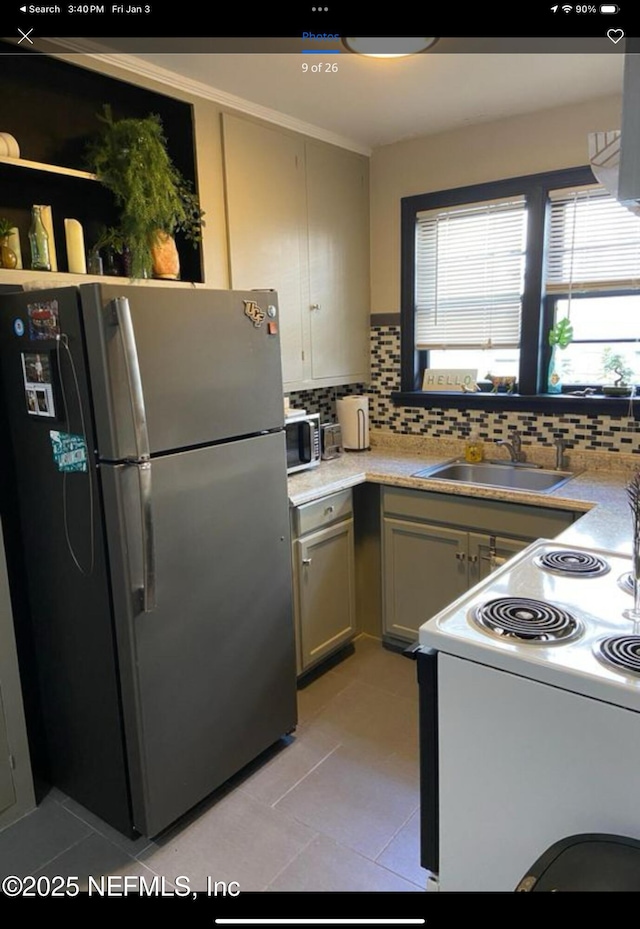 kitchen featuring stove, sink, light tile patterned floors, tasteful backsplash, and stainless steel refrigerator