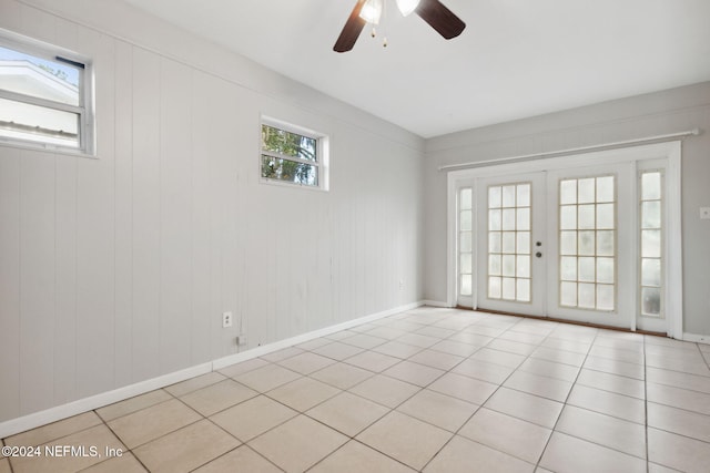 tiled empty room featuring a wealth of natural light, french doors, ceiling fan, and wood walls