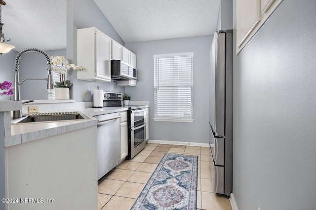 kitchen with appliances with stainless steel finishes, vaulted ceiling, white cabinetry, hanging light fixtures, and light tile patterned flooring