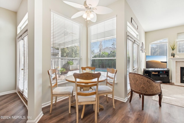 dining area featuring a tiled fireplace, ceiling fan, and dark wood-type flooring