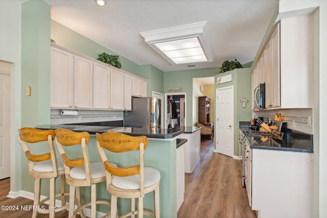 kitchen featuring kitchen peninsula, appliances with stainless steel finishes, a kitchen breakfast bar, and hardwood / wood-style floors