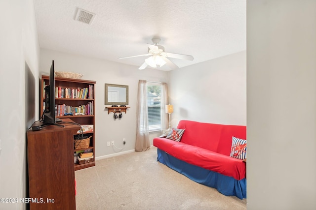 living area with light carpet, ceiling fan, and a textured ceiling