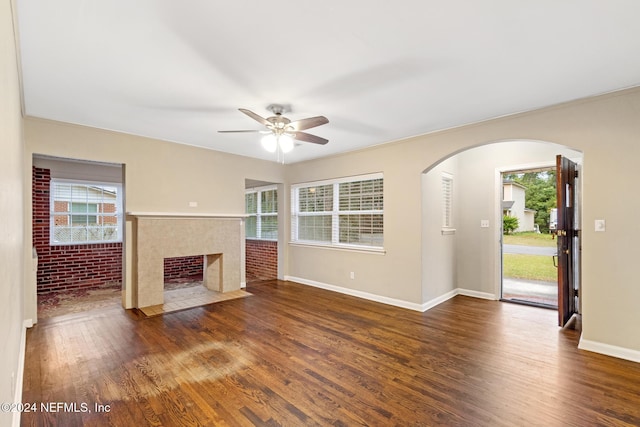 unfurnished living room with dark hardwood / wood-style floors, ceiling fan, and brick wall