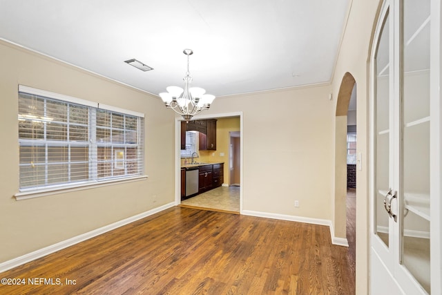 unfurnished dining area featuring dark hardwood / wood-style floors, crown molding, a notable chandelier, and sink