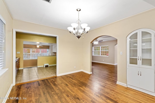 unfurnished dining area featuring hardwood / wood-style floors, plenty of natural light, ornamental molding, and ceiling fan with notable chandelier