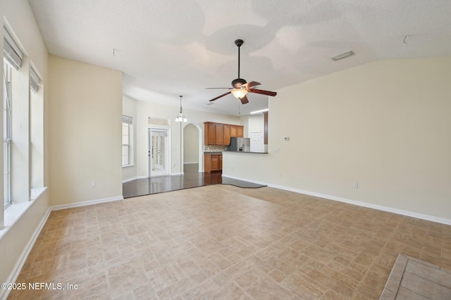 unfurnished living room featuring a wealth of natural light, a textured ceiling, ceiling fan, and lofted ceiling