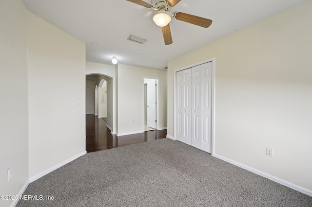 unfurnished bedroom with ceiling fan, a closet, and dark colored carpet