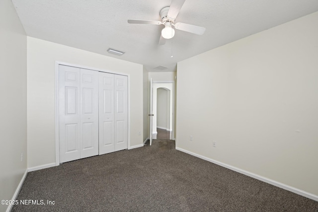 unfurnished bedroom featuring ceiling fan, a closet, a textured ceiling, and dark colored carpet