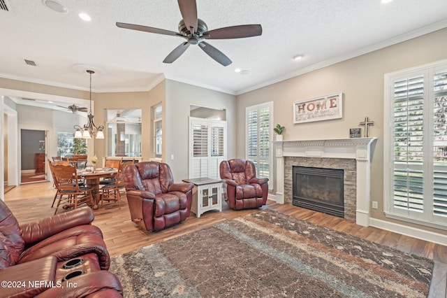 living room with light hardwood / wood-style floors, a textured ceiling, a fireplace, ceiling fan with notable chandelier, and ornamental molding