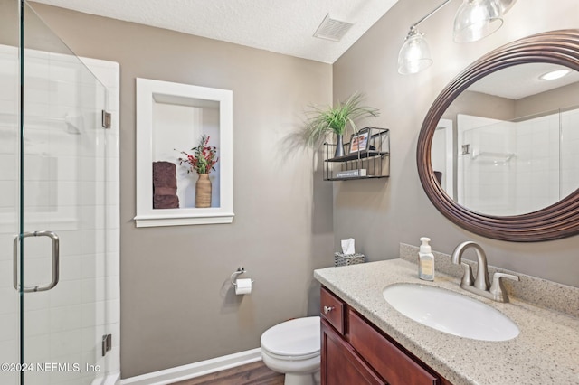 bathroom featuring vanity, a textured ceiling, a shower with door, hardwood / wood-style floors, and toilet