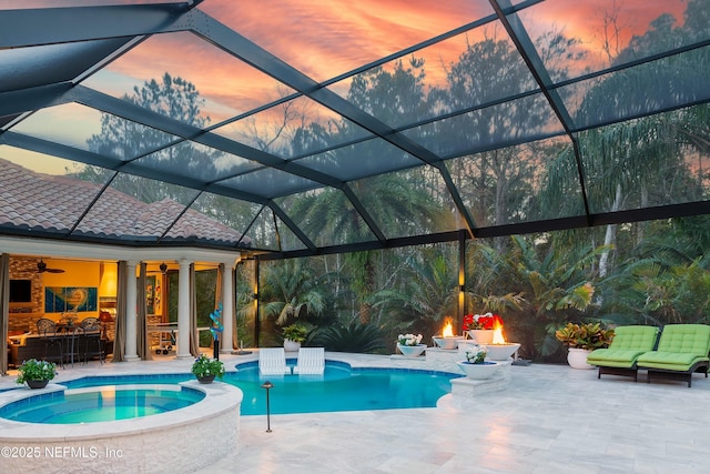 pool at dusk featuring glass enclosure, an in ground hot tub, a patio area, and ceiling fan