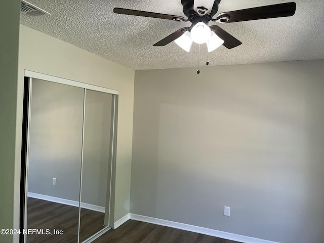 unfurnished bedroom featuring ceiling fan, a closet, dark wood-type flooring, and a textured ceiling