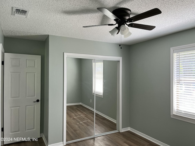 unfurnished bedroom with a textured ceiling, ceiling fan, dark wood-type flooring, and a closet