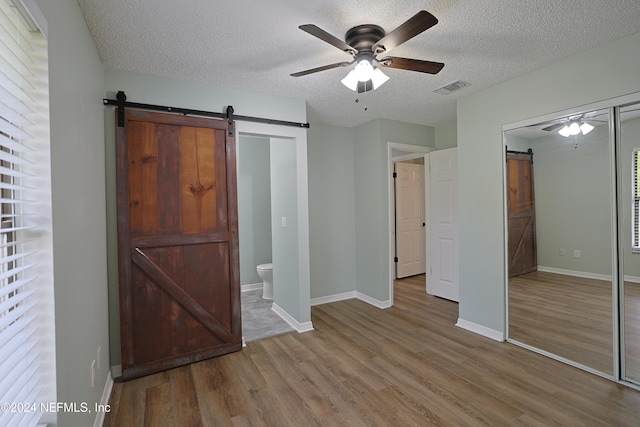 unfurnished bedroom featuring connected bathroom, ceiling fan, a barn door, hardwood / wood-style floors, and a textured ceiling