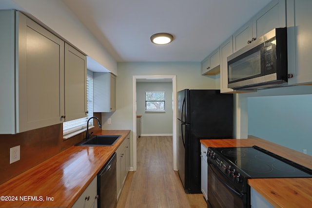 kitchen with sink, light hardwood / wood-style flooring, black appliances, and wood counters