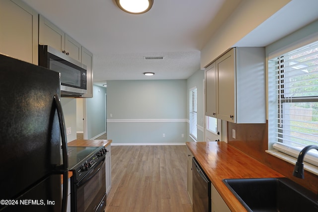 kitchen with butcher block counters, a wealth of natural light, sink, and black appliances