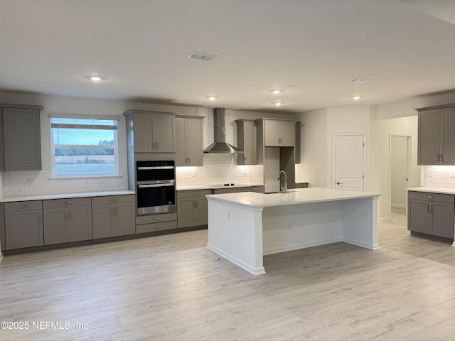 kitchen featuring gray cabinetry, black electric stovetop, double oven, wall chimney exhaust hood, and a sink