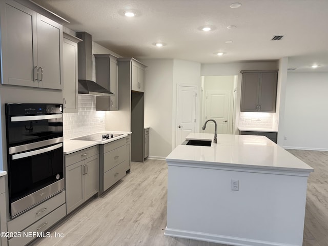 kitchen featuring gray cabinets, a sink, double oven, wall chimney range hood, and black electric cooktop