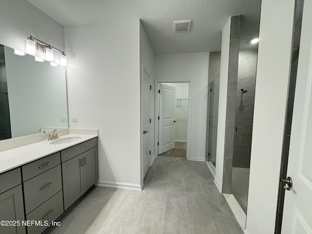 full bath with vanity, baseboards, visible vents, a stall shower, and a textured ceiling