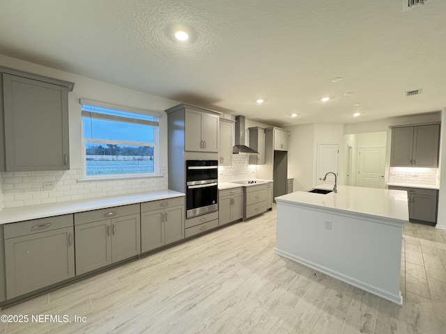 kitchen with gray cabinets, a sink, double oven, wall chimney exhaust hood, and black electric stovetop