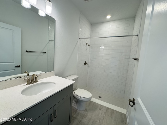 full bath featuring tiled shower, toilet, wood finished floors, and vanity