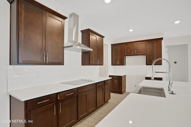 kitchen featuring black electric stovetop, wall chimney exhaust hood, sink, and dark brown cabinets