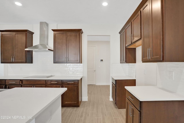 kitchen featuring backsplash, black electric stovetop, dark brown cabinets, wall chimney range hood, and light wood-type flooring