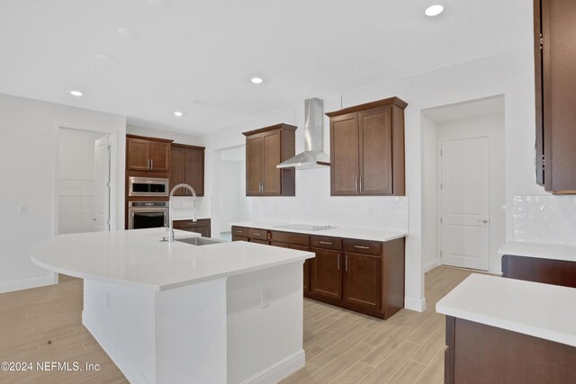 kitchen featuring an island with sink, appliances with stainless steel finishes, sink, and wall chimney range hood