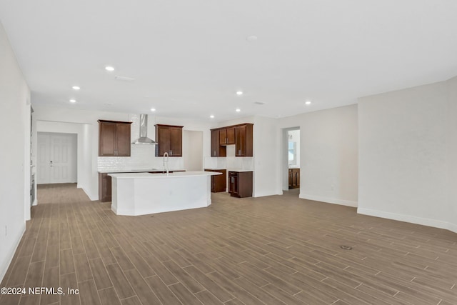 kitchen with tasteful backsplash, sink, a kitchen island with sink, wall chimney exhaust hood, and light hardwood / wood-style flooring