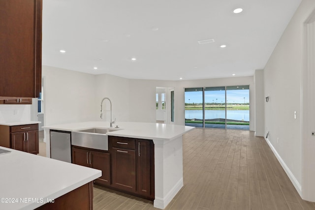 kitchen with an island with sink, a water view, sink, and dishwashing machine