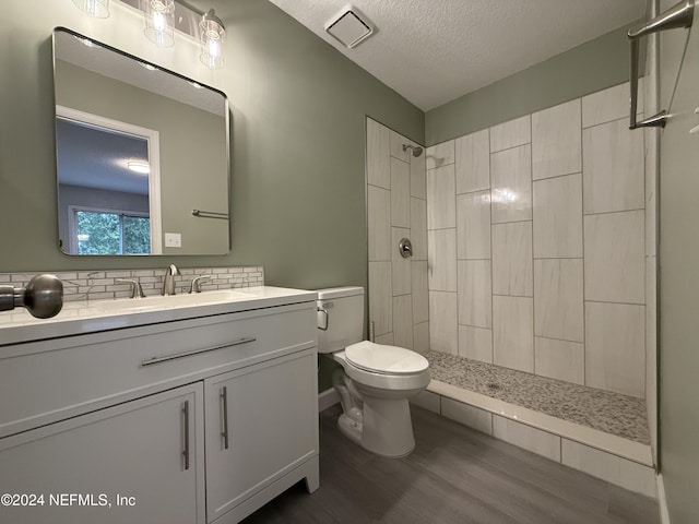 bathroom featuring a tile shower, hardwood / wood-style floors, a textured ceiling, toilet, and vanity