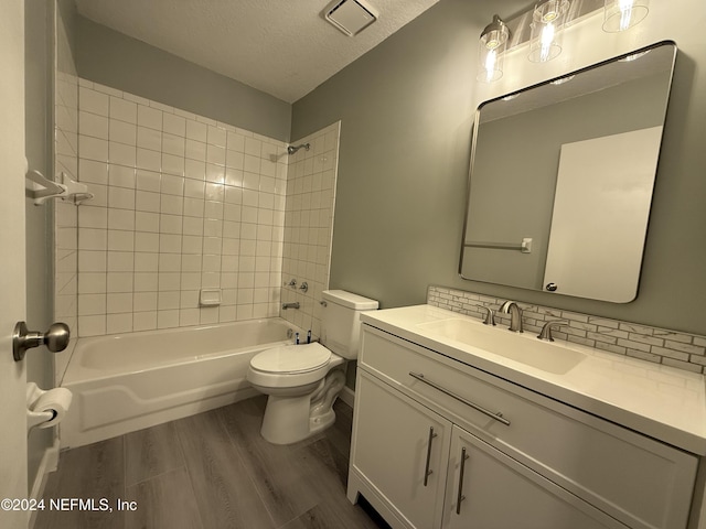 full bathroom with tiled shower / bath combo, wood-type flooring, a textured ceiling, toilet, and vanity