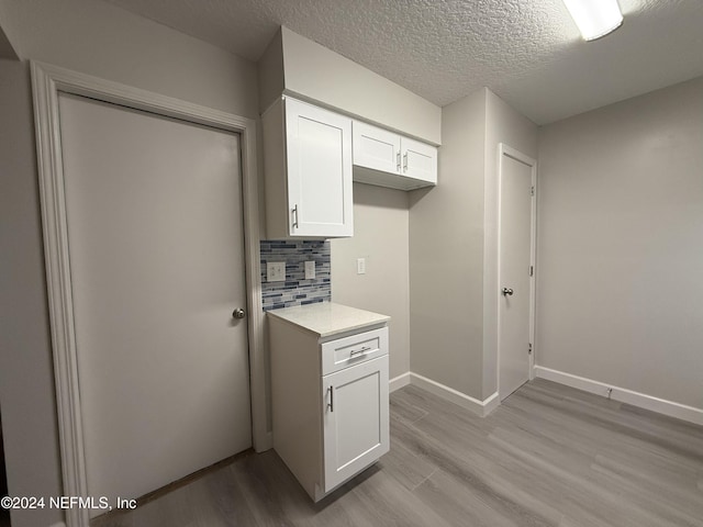 kitchen featuring white cabinets, light hardwood / wood-style floors, backsplash, and a textured ceiling